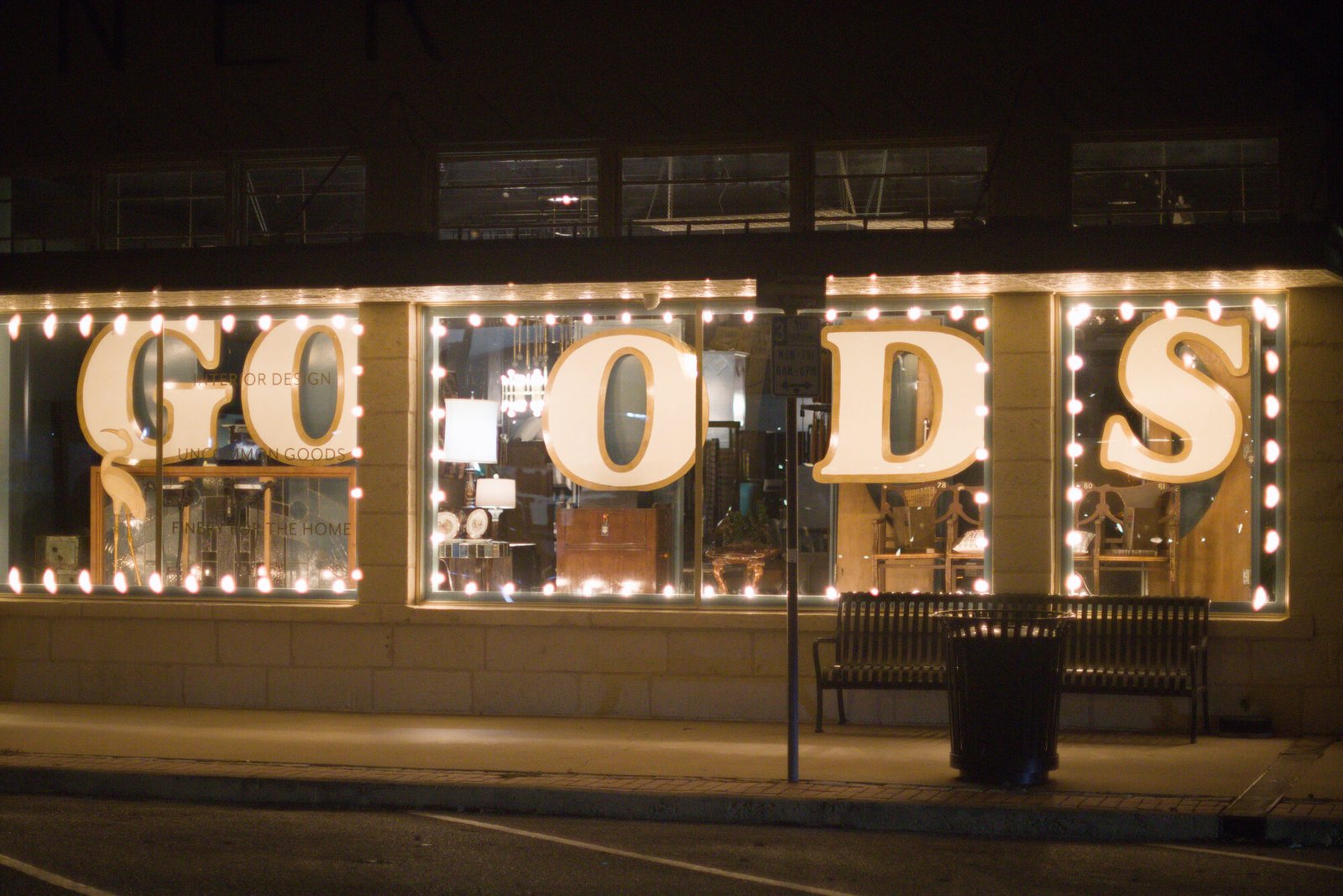 A downtown Kerrville shop window before dawn, the word GOODS spelled out in lit marquee letters